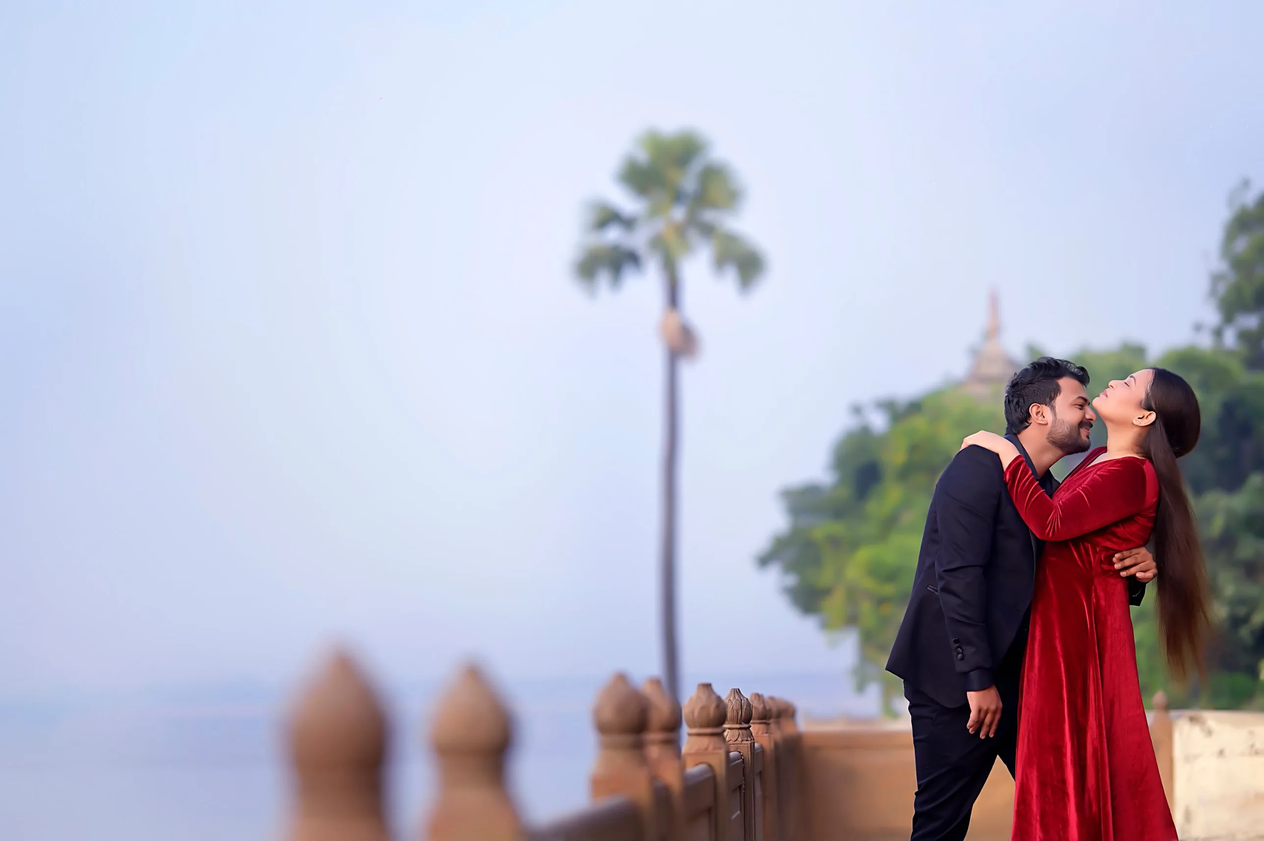 Couple embracing by the river ghat, bride in a red velvet gown