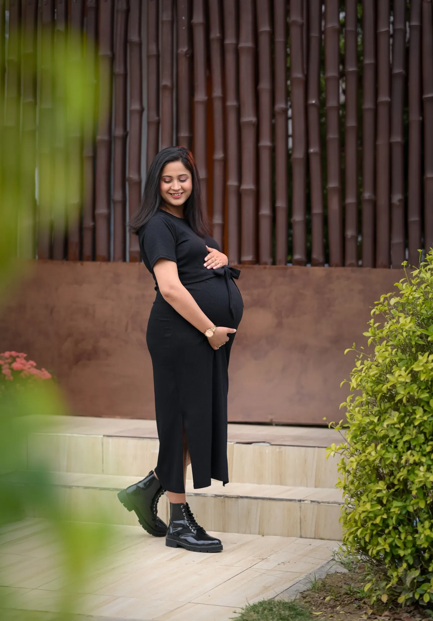 Mother-to-be in a black dress against a bamboo wall