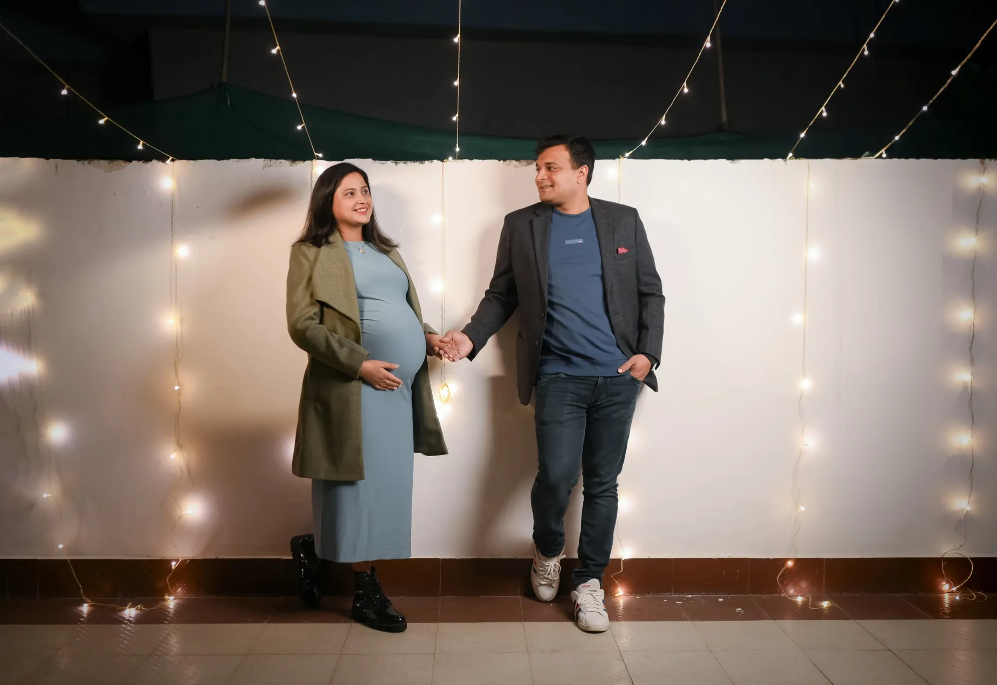 Expecting couple holding hands under twinkling strings