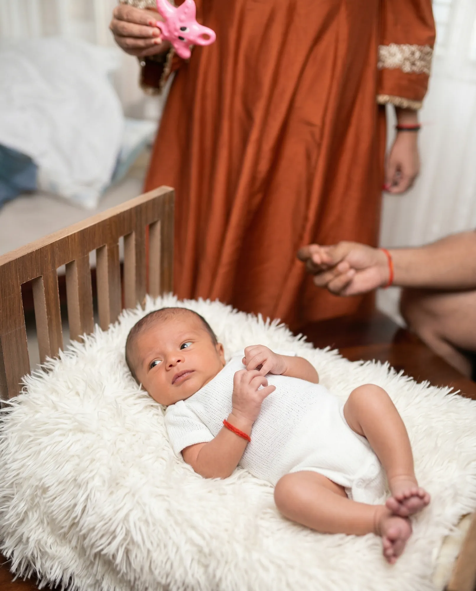 Newborn awake on a fur throw as parents play with him
