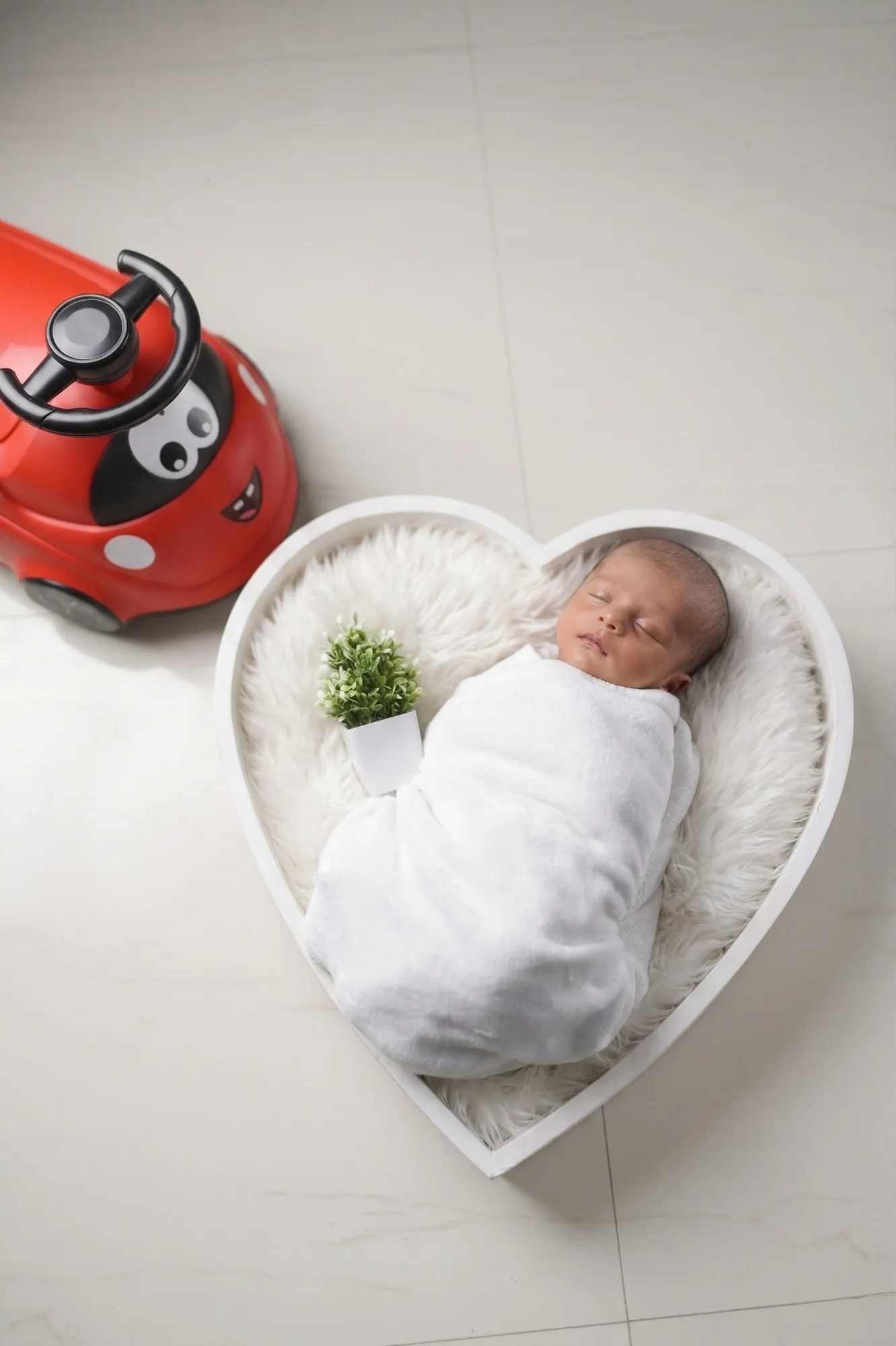 Newborn in a heart-shaped bed beside a red toy car