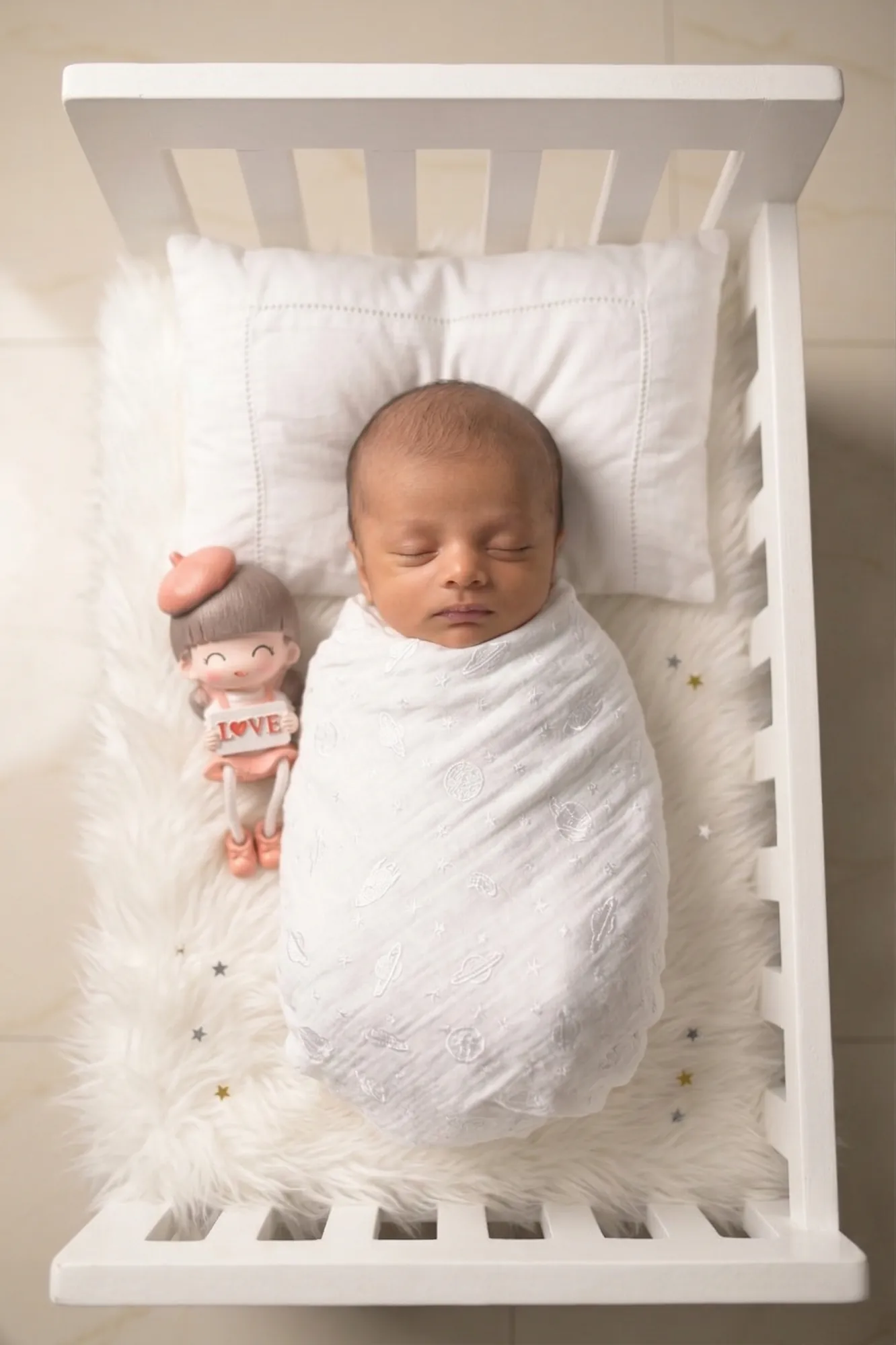 Newborn asleep in a white crib with a little doll