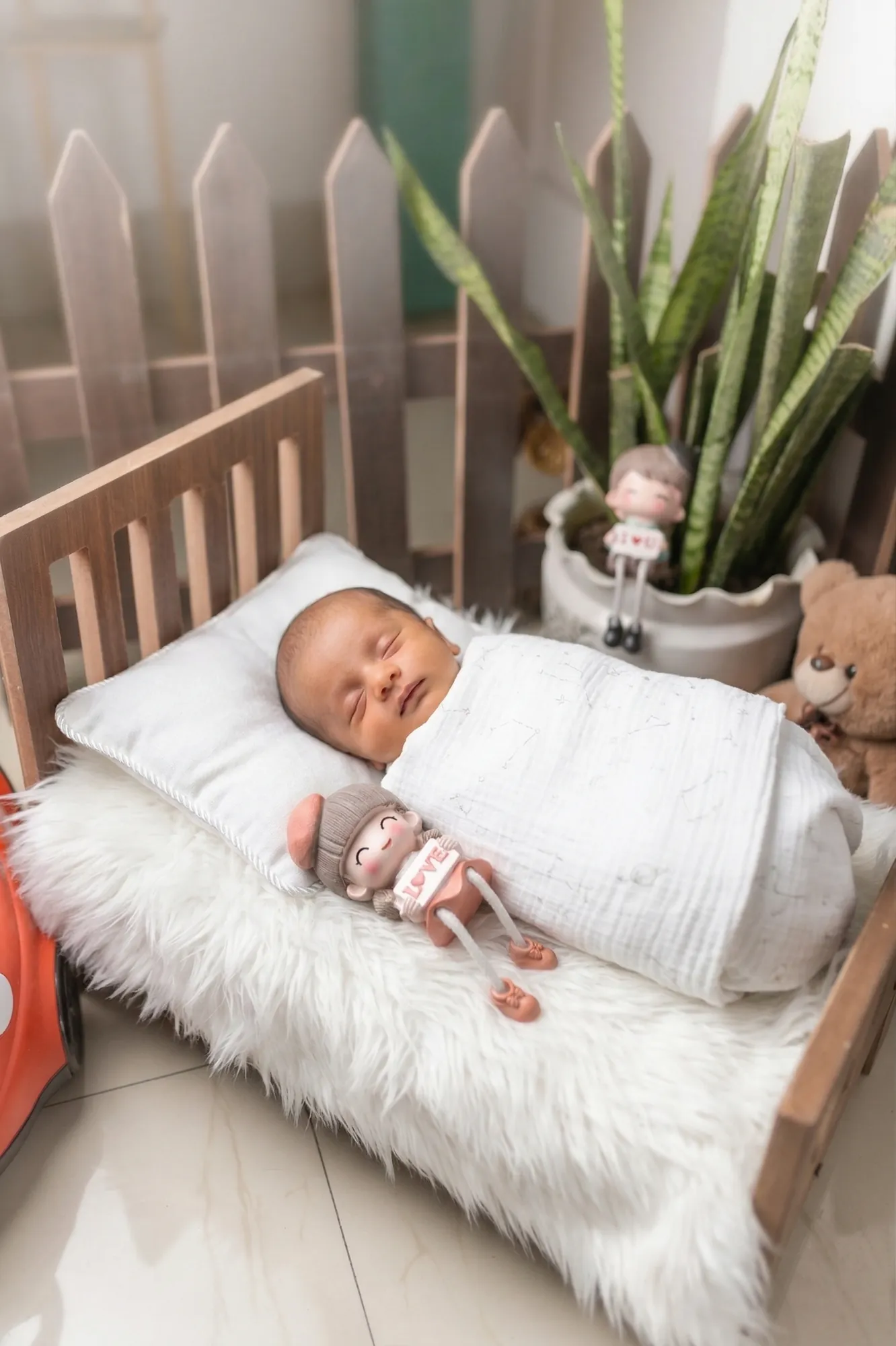 Newborn asleep on a little wooden bed with props