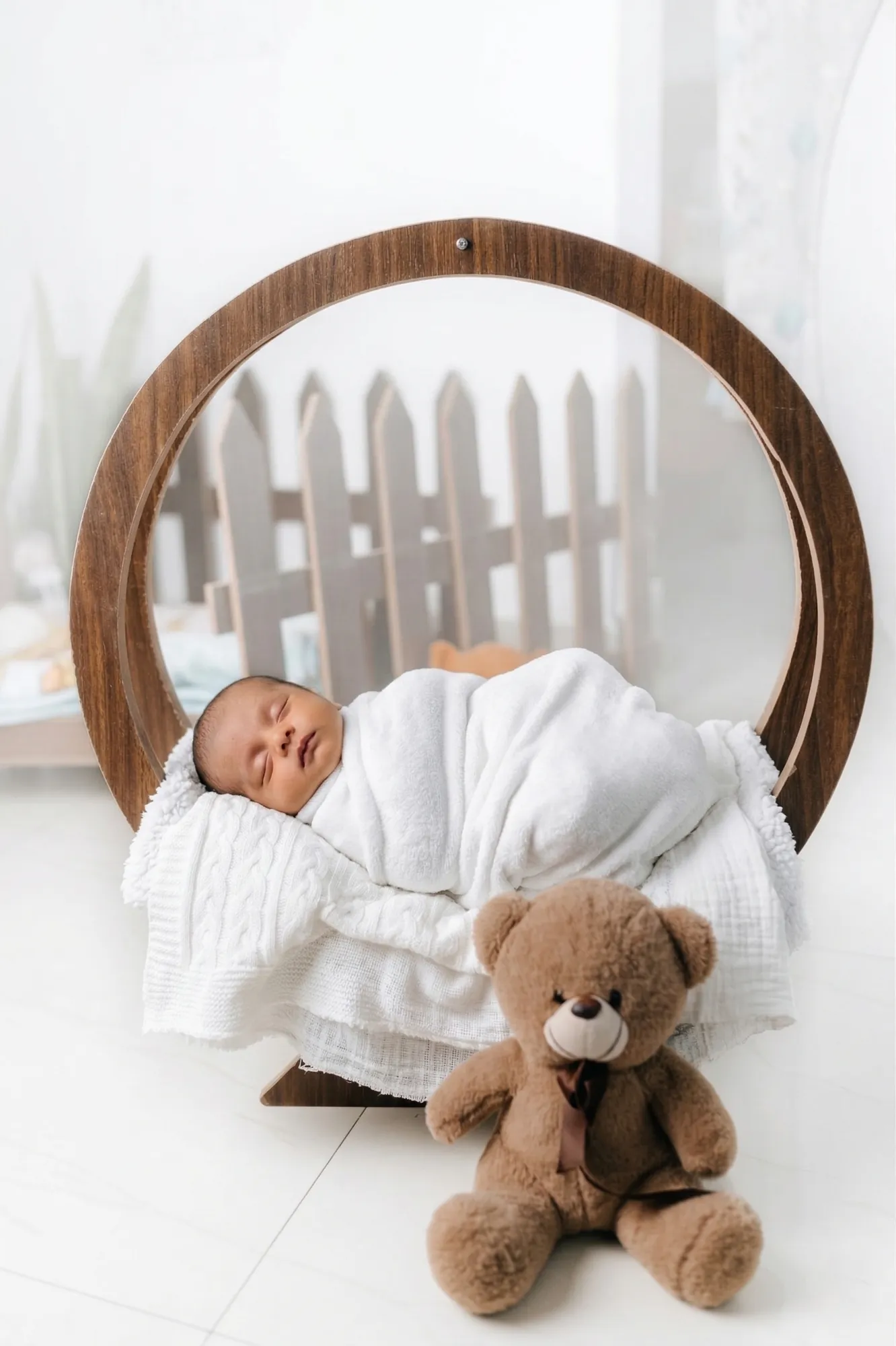 Newborn asleep in a wooden ring with a teddy bear