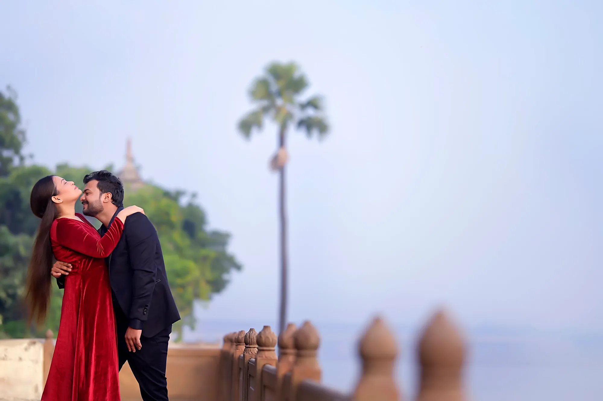 Pre-wedding couple at a riverside ghat, bride in a red velvet gown
