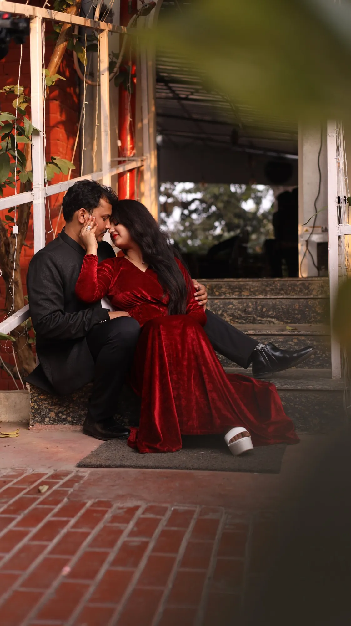 Pre-wedding couple in red velvet and a black suit on brick steps